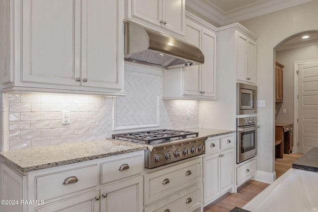 kitchen with tasteful backsplash, ornamental molding, stainless steel appliances, light hardwood / wood-style flooring, and white cabinetry