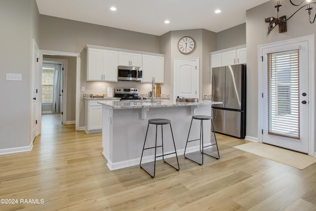 kitchen featuring an island with sink, white cabinets, stainless steel appliances, and light hardwood / wood-style floors