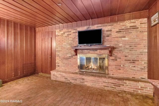 unfurnished living room with wooden ceiling, wooden walls, a brick fireplace, and brick floor