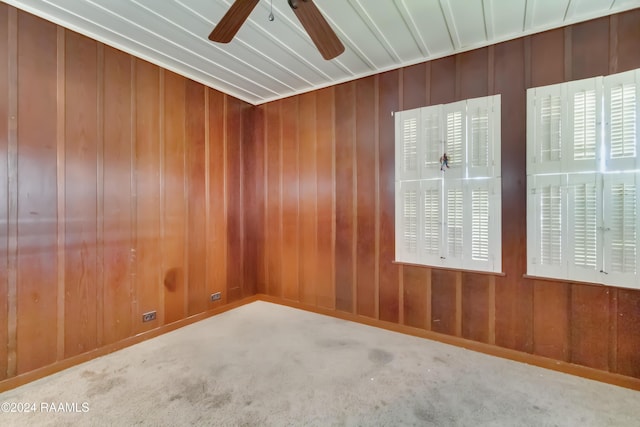 carpeted empty room featuring wooden walls and ceiling fan