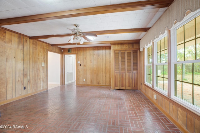 empty room featuring beamed ceiling, ceiling fan, and wood walls