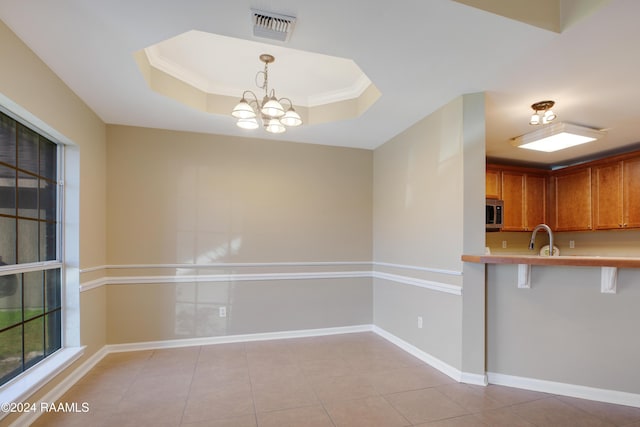 kitchen featuring an inviting chandelier, sink, a tray ceiling, decorative light fixtures, and a breakfast bar area