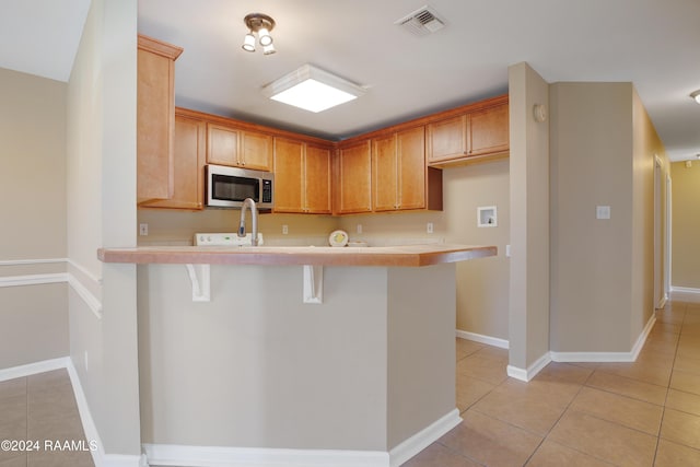 kitchen with kitchen peninsula, light tile patterned floors, and a breakfast bar area