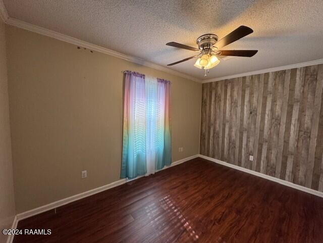 empty room with a textured ceiling, dark hardwood / wood-style flooring, ornamental molding, and wood walls