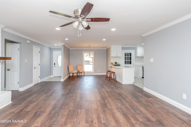 unfurnished living room featuring ceiling fan with notable chandelier, crown molding, and dark wood-type flooring