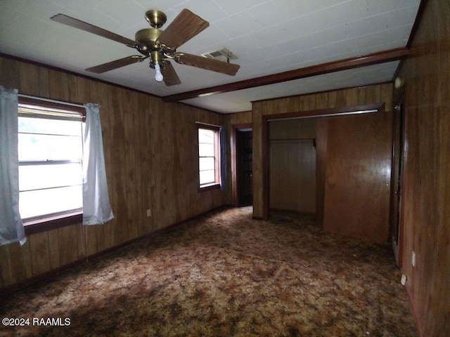 unfurnished bedroom featuring dark colored carpet, ceiling fan, a closet, and wood walls