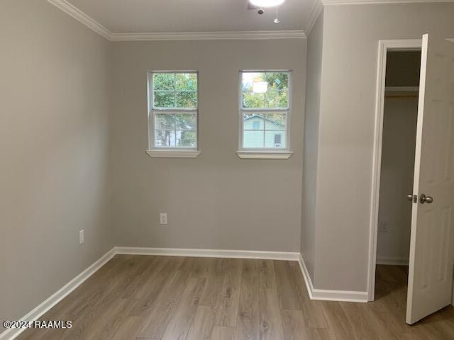 unfurnished bedroom featuring crown molding, a closet, baseboards, and wood finished floors