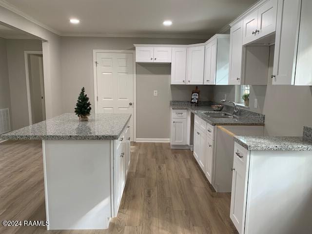 kitchen featuring a center island, crown molding, white cabinets, a sink, and wood finished floors