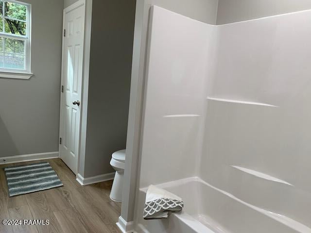 bathroom with toilet, baseboards, wood finished floors, and shower / bathtub combination