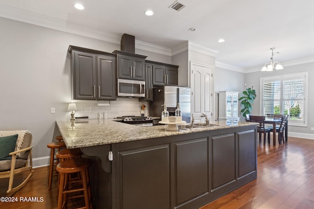 kitchen featuring dark hardwood / wood-style flooring, ornamental molding, stainless steel appliances, and an inviting chandelier