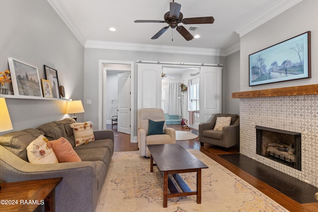 living room with a tiled fireplace, a barn door, ornamental molding, and hardwood / wood-style flooring