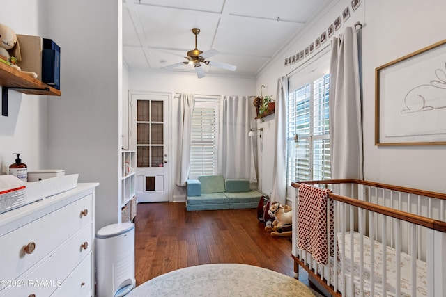 bedroom featuring ceiling fan, dark wood-type flooring, coffered ceiling, a nursery area, and ornamental molding