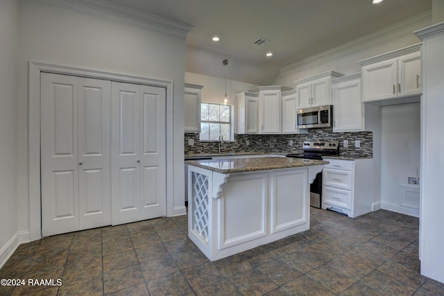 kitchen with a center island, dark stone countertops, appliances with stainless steel finishes, white cabinets, and ornamental molding