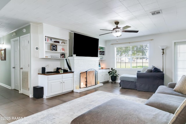 living room featuring a fireplace, built in shelves, dark tile patterned floors, and ceiling fan