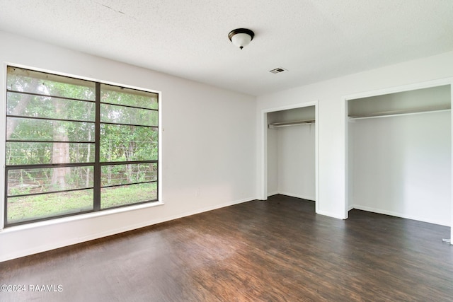 unfurnished bedroom featuring a textured ceiling, dark hardwood / wood-style floors, multiple windows, and multiple closets