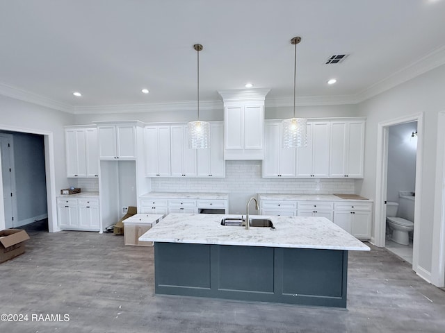 kitchen featuring a kitchen island with sink, sink, decorative light fixtures, and white cabinets