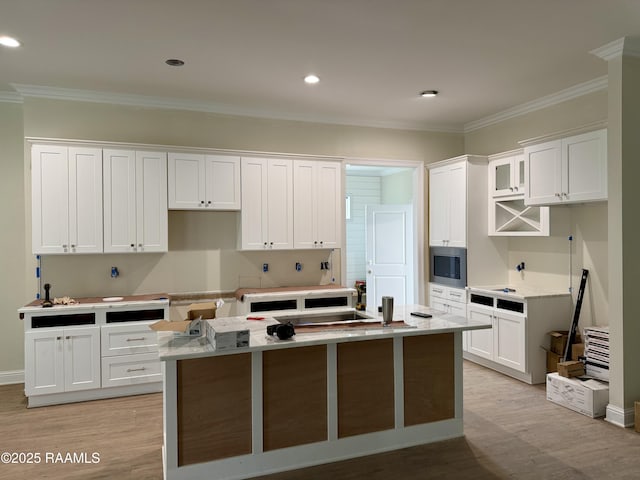 kitchen with white cabinets, light hardwood / wood-style flooring, a kitchen island with sink, and crown molding