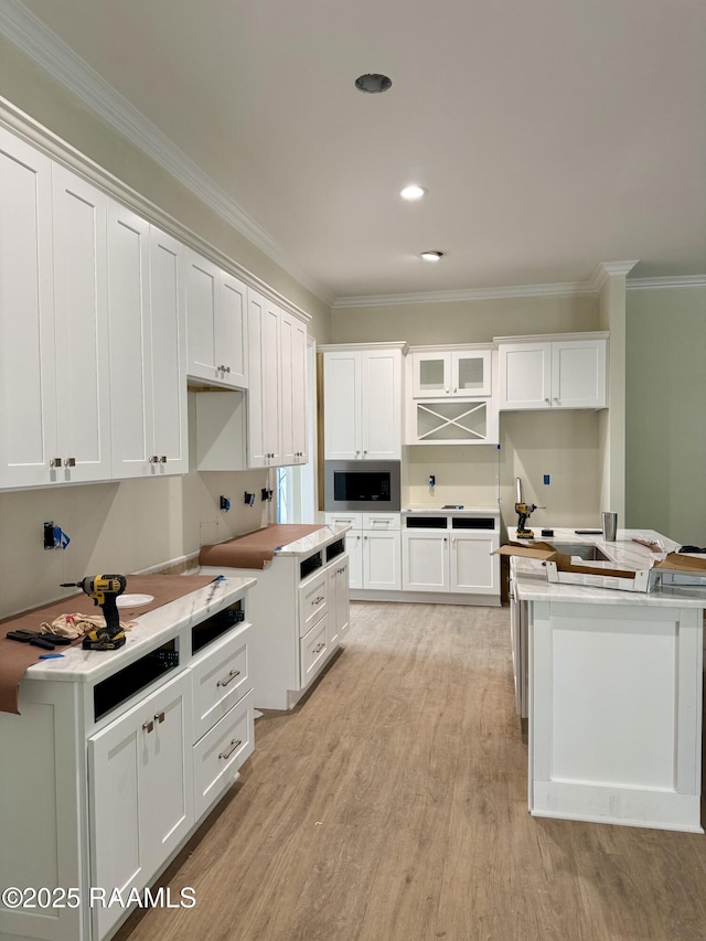 kitchen with white cabinets, light wood-type flooring, crown molding, and stainless steel microwave