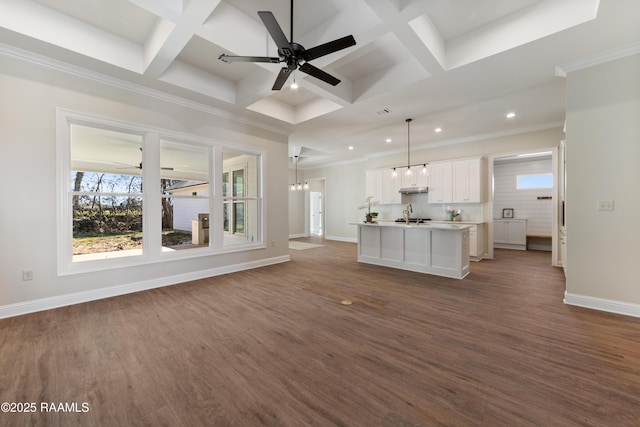 unfurnished living room with dark wood-style flooring, a sink, coffered ceiling, baseboards, and ceiling fan with notable chandelier