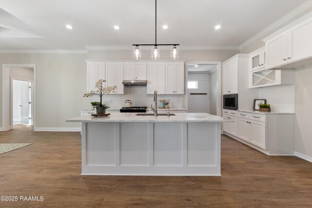 kitchen with white cabinets, dark wood-type flooring, light countertops, under cabinet range hood, and a sink