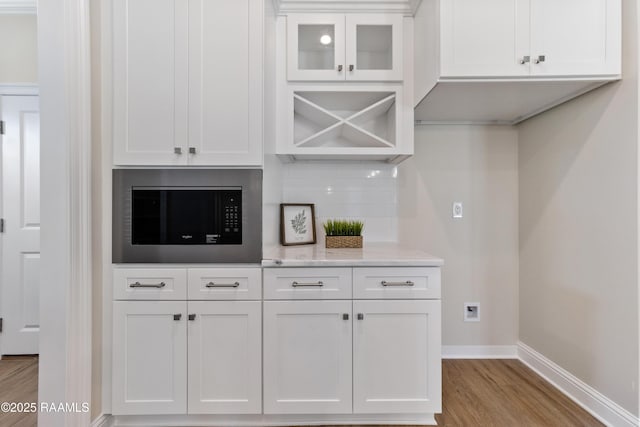 kitchen featuring tasteful backsplash, white cabinetry, wood finished floors, built in microwave, and baseboards