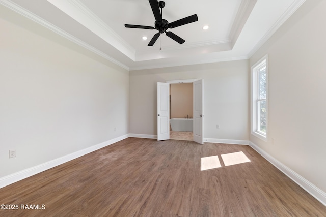 unfurnished bedroom with a tray ceiling, crown molding, recessed lighting, wood finished floors, and baseboards