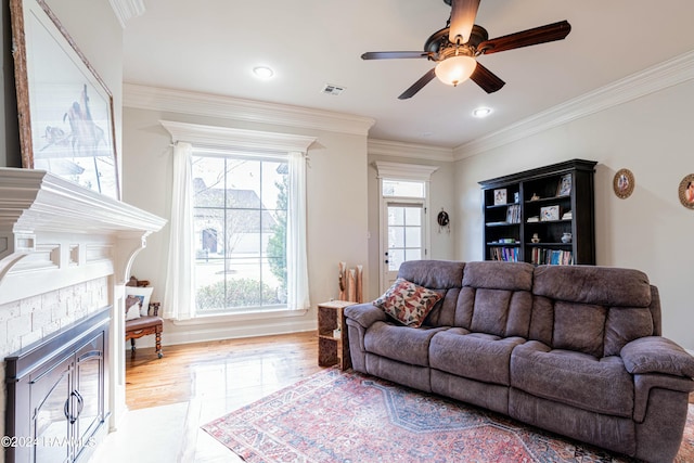 living room featuring ceiling fan, a fireplace, ornamental molding, and light wood-type flooring