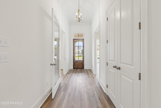 doorway featuring baseboards, crown molding, a chandelier, and light wood-style flooring
