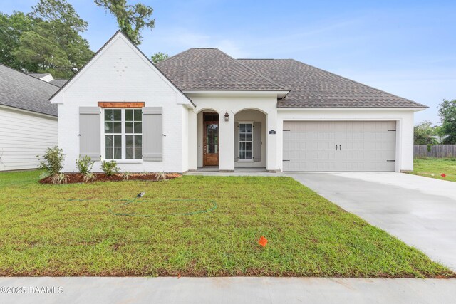 view of front of property featuring a front lawn, an attached garage, driveway, brick siding, and roof with shingles