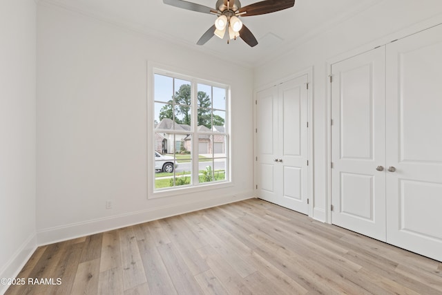 unfurnished bedroom with a ceiling fan, crown molding, two closets, light wood finished floors, and baseboards