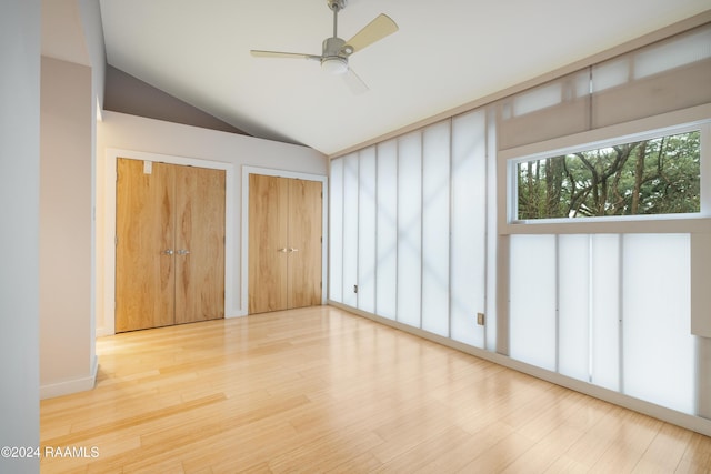 unfurnished bedroom with hardwood / wood-style floors, two closets, vaulted ceiling, and ceiling fan