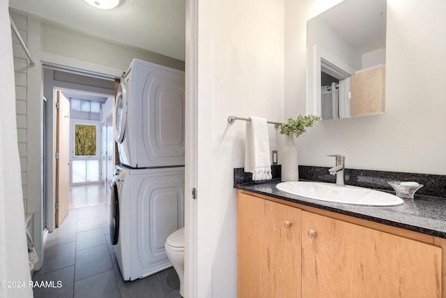 bathroom with tile patterned flooring, vanity, stacked washer and clothes dryer, and toilet