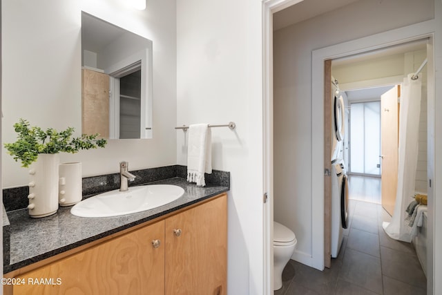 bathroom featuring tile patterned floors, vanity, toilet, and stacked washer / dryer