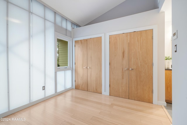 unfurnished bedroom featuring multiple closets, wood-type flooring, and vaulted ceiling