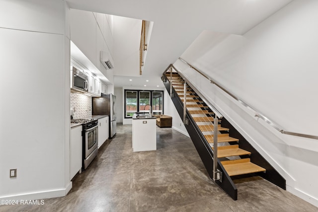 1611 W University Ave, Lafayette, LA 70506 - kitchen with stainless steel appliances, a wall mounted air conditioner, white cabinets, an island with sink, and backsplash