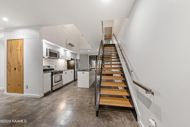 staircase with a wall mounted air conditioner, concrete flooring, and sink