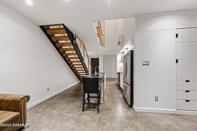 kitchen with stainless steel refrigerator, white cabinetry, sink, an AC wall unit, and a kitchen bar