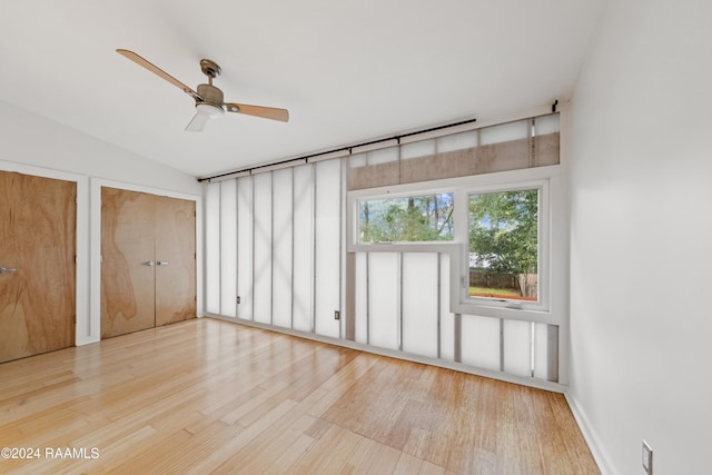 unfurnished bedroom featuring multiple closets, ceiling fan, vaulted ceiling, and light wood-type flooring