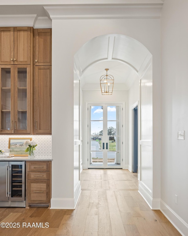 interior space featuring backsplash, baseboards, wine cooler, ornamental molding, and light wood-style flooring