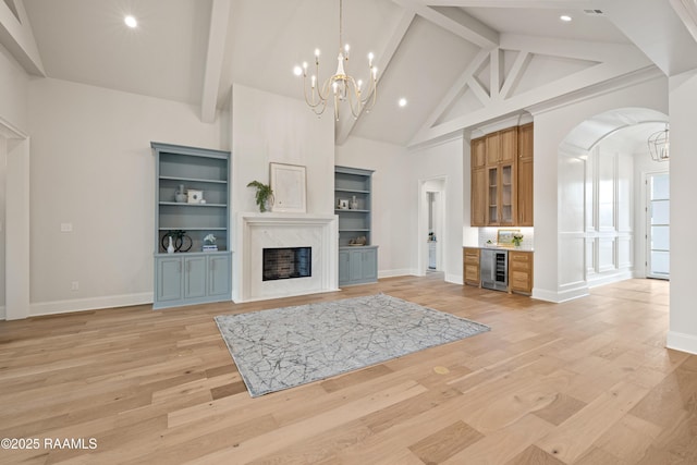 unfurnished living room featuring light wood finished floors, beam ceiling, high vaulted ceiling, and a high end fireplace