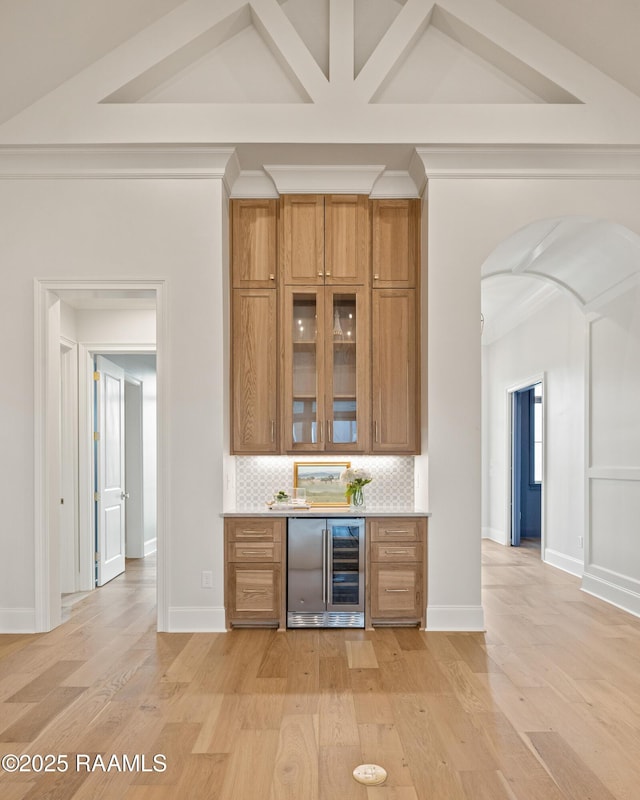 bar featuring light wood finished floors, backsplash, beverage cooler, arched walkways, and a bar