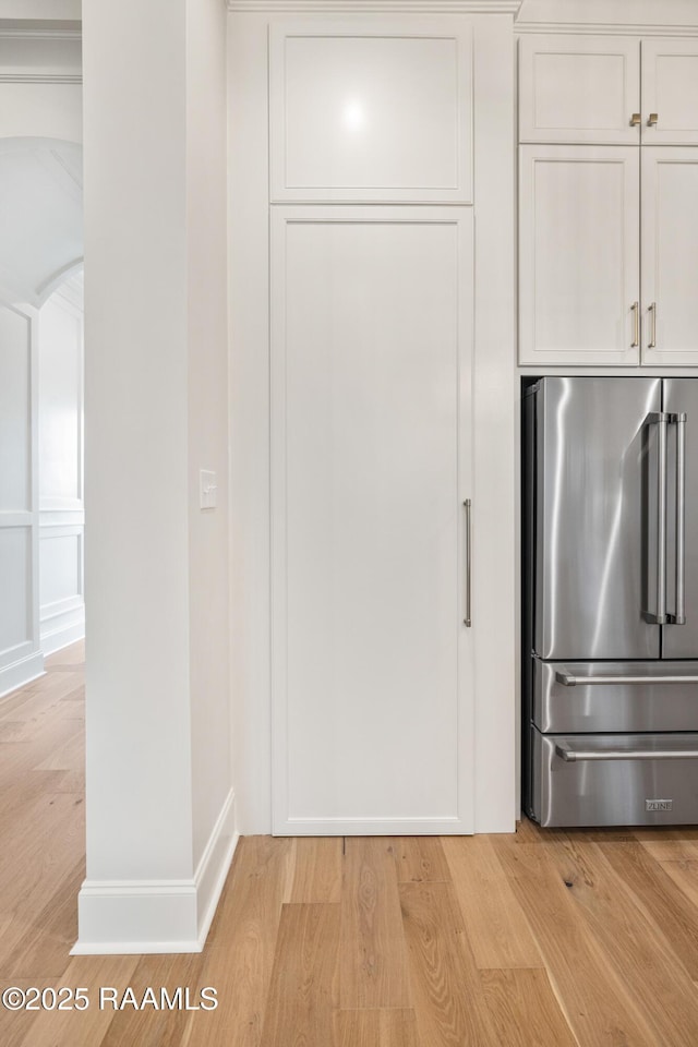 kitchen with white cabinetry, light wood finished floors, arched walkways, and freestanding refrigerator