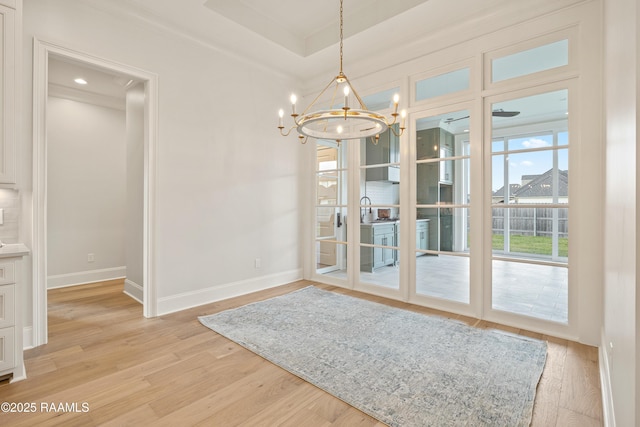 interior space featuring a notable chandelier, light wood-style flooring, a raised ceiling, and baseboards