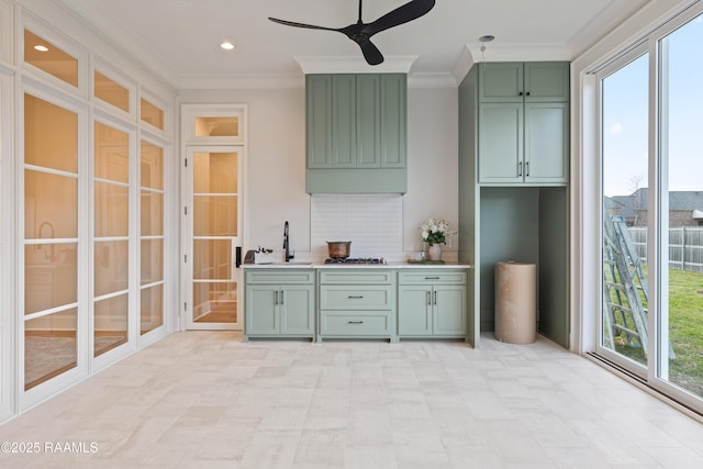 kitchen featuring green cabinets, ceiling fan, ornamental molding, decorative backsplash, and a sink