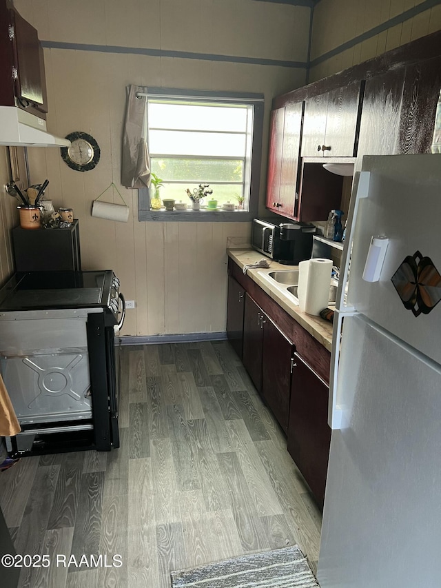 kitchen featuring wood walls, black electric range, light wood-type flooring, white fridge, and dark brown cabinetry