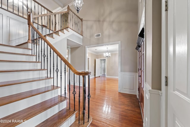 staircase featuring wood-type flooring, ornamental molding, a towering ceiling, and a chandelier