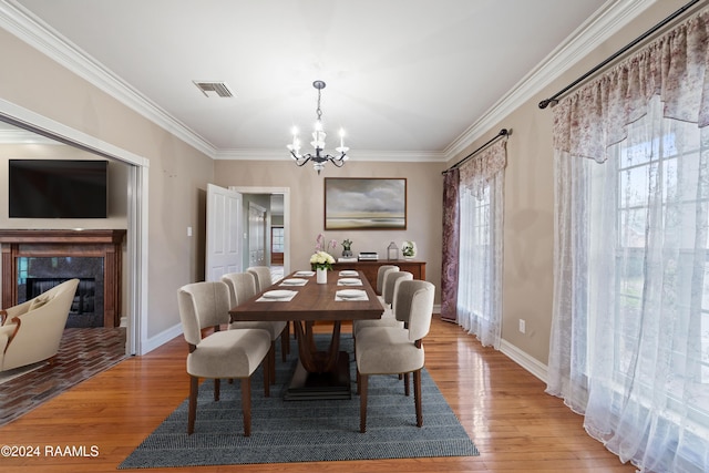 dining room featuring light wood-type flooring, a premium fireplace, crown molding, and a notable chandelier