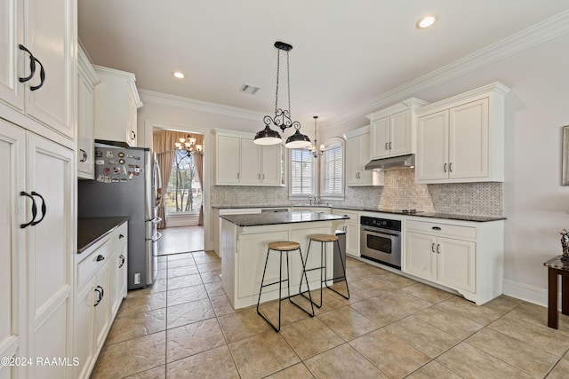 kitchen with appliances with stainless steel finishes, ornamental molding, decorative light fixtures, white cabinets, and a center island