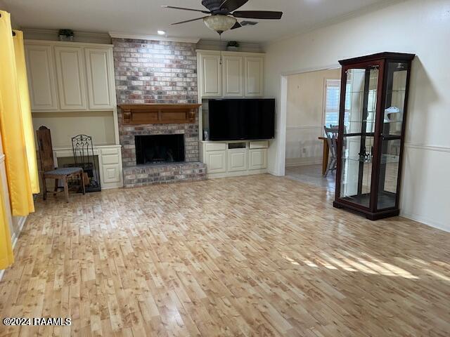 unfurnished living room featuring ceiling fan, light wood-type flooring, ornamental molding, and a brick fireplace