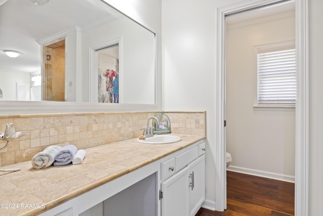 bathroom with tasteful backsplash, wood-type flooring, toilet, vanity, and ornamental molding